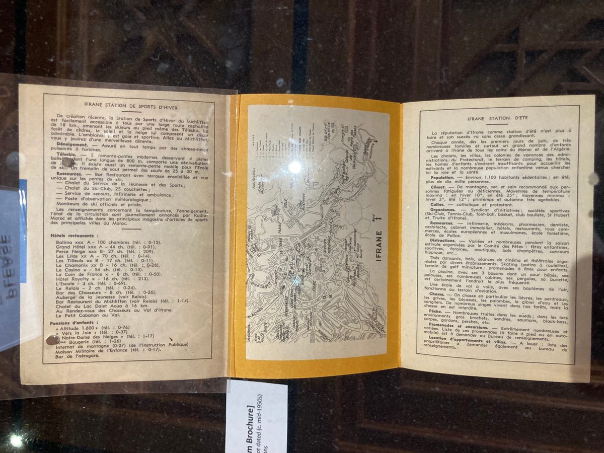 Display case at Mohammed VI Library, Al-Akhawayn University in Ifrane, Morocco, showing archival materials including postcards, letters, advertisements, vacation photos, and maps from the colonial and postcolonial period.