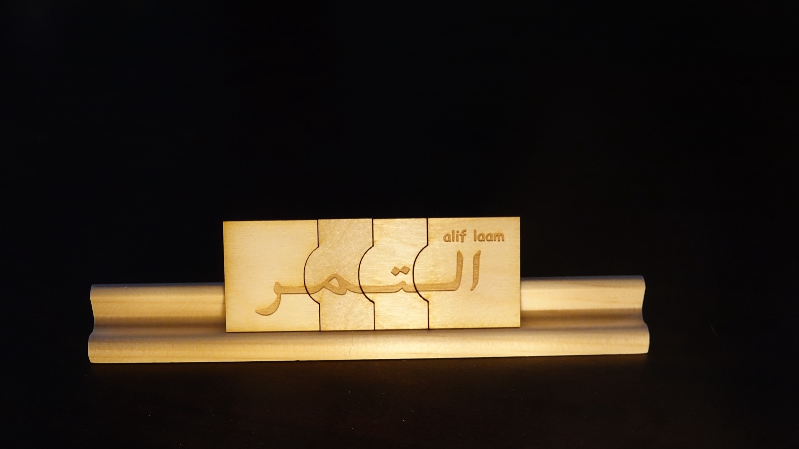Close detail of a Huruf La'b laser-cut wooden puzzle spelling an Arabic word on its stand against a dark background.